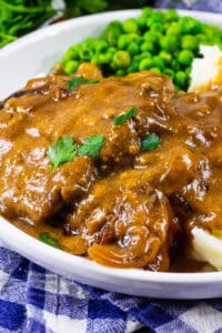 Crock Pot Cubed Steak with Gravy on a plate with mashed potatoes and peas.