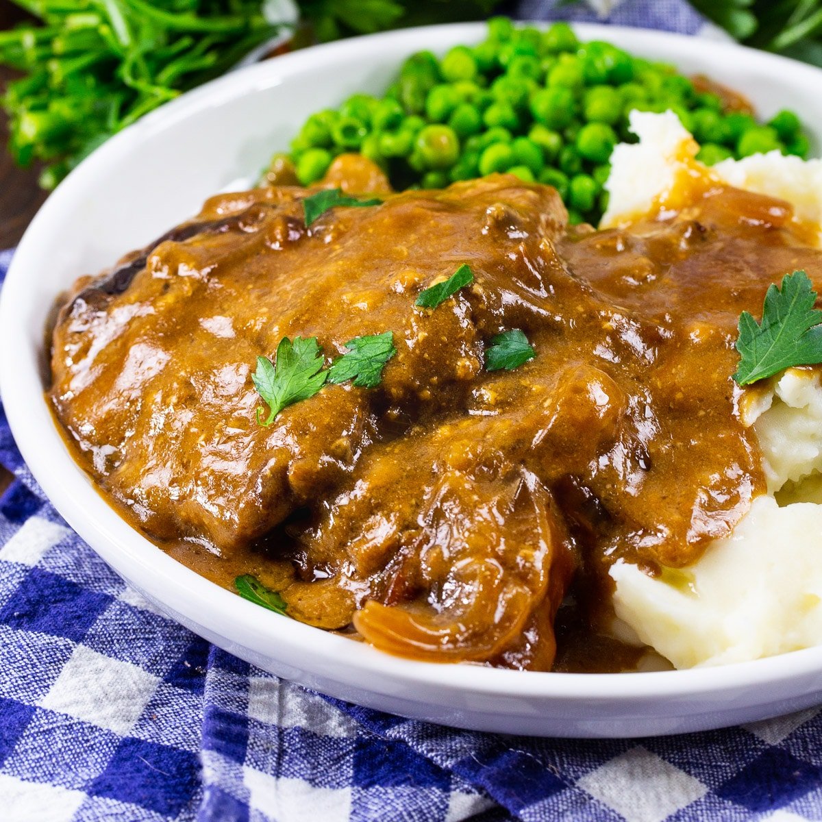 Crock Pot Cubed Steak with Gravy on a plate with mashed potatoes and peas.