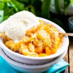 Slow Cooker Peach Cobbler topped with vanilla ice cream in a bowl.