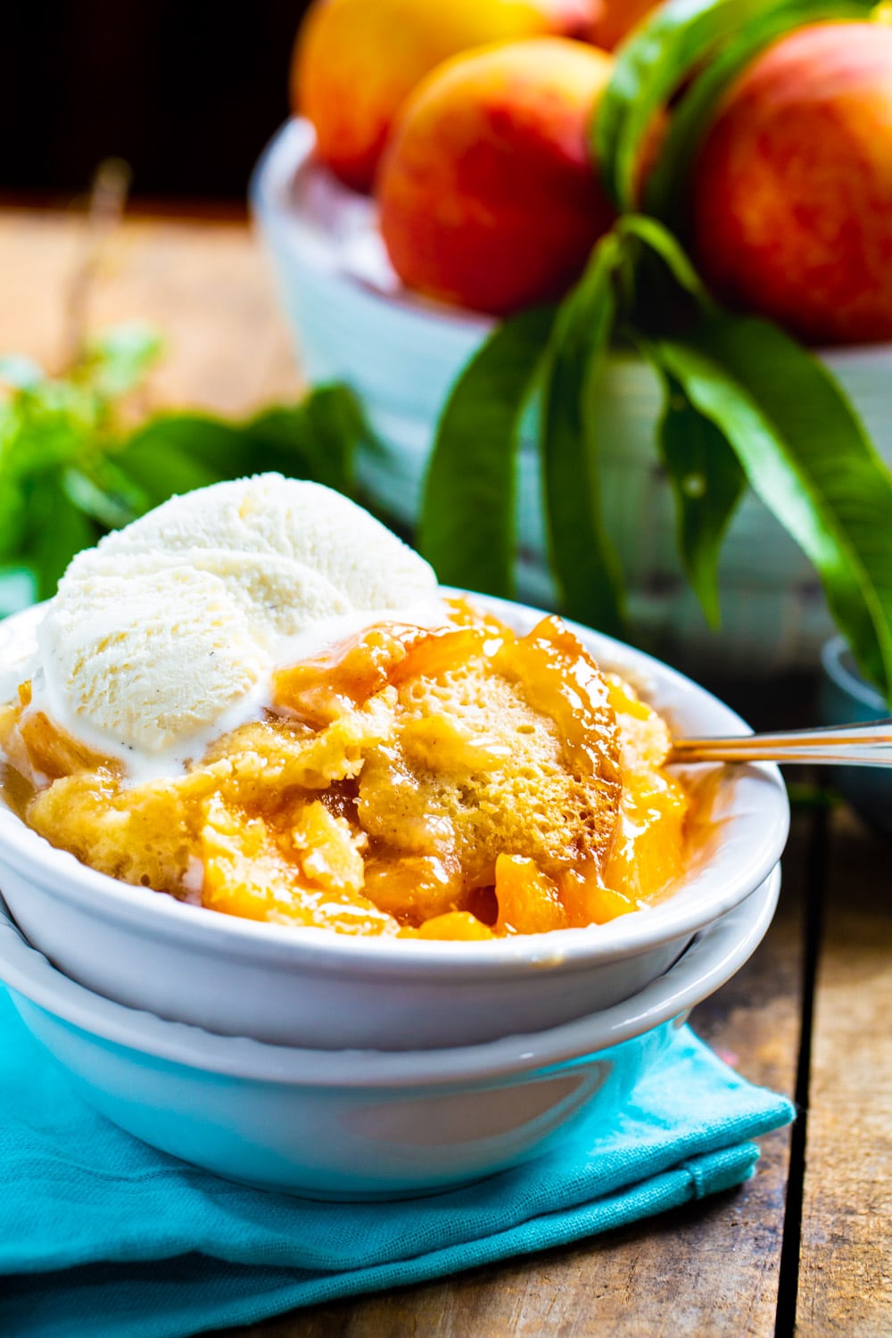 Peach Cobbler in bowl with ice cream. Bowl of peaches in background.