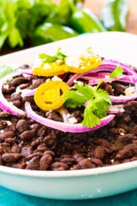 Spicy Black Beans in white bowl, topped with red onion and cilantro.