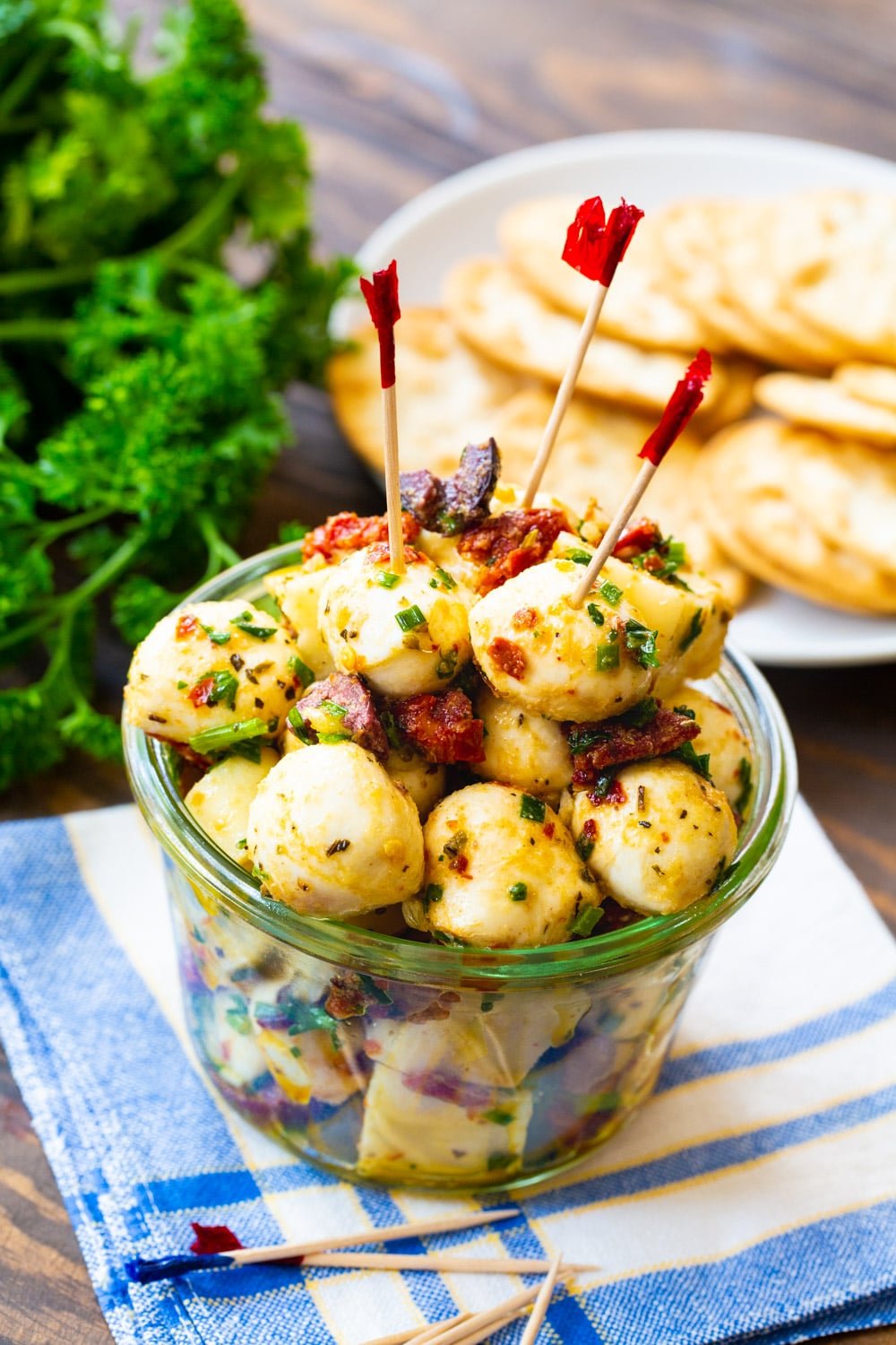 Jar full of marinated mozzarella balls with crackers and parsley in background.