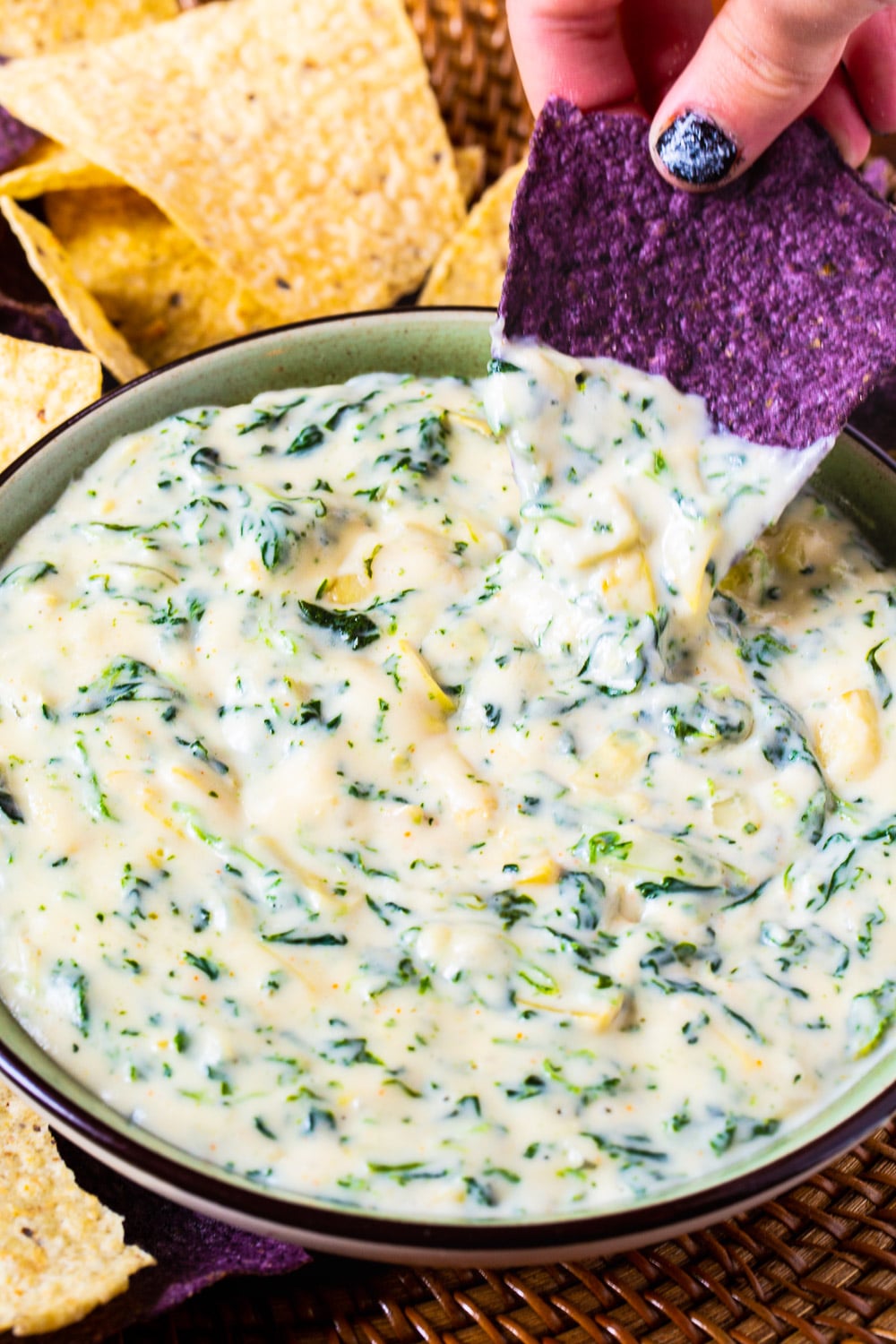 Spinach Dip in a bowl beinf scooped by a tortilla chip.