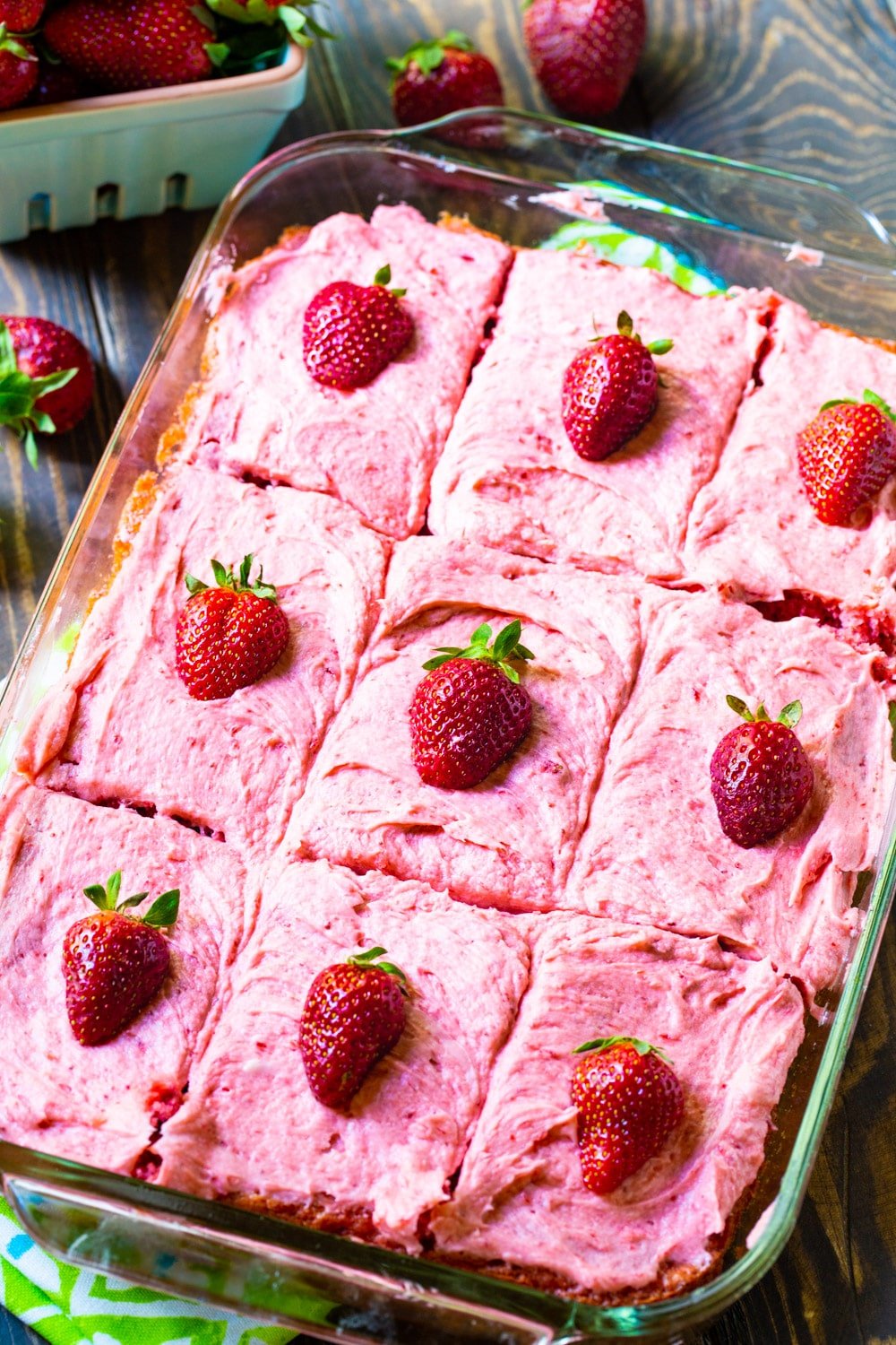 Strawberry flavored sheet cake cut into squares in a baking pan.