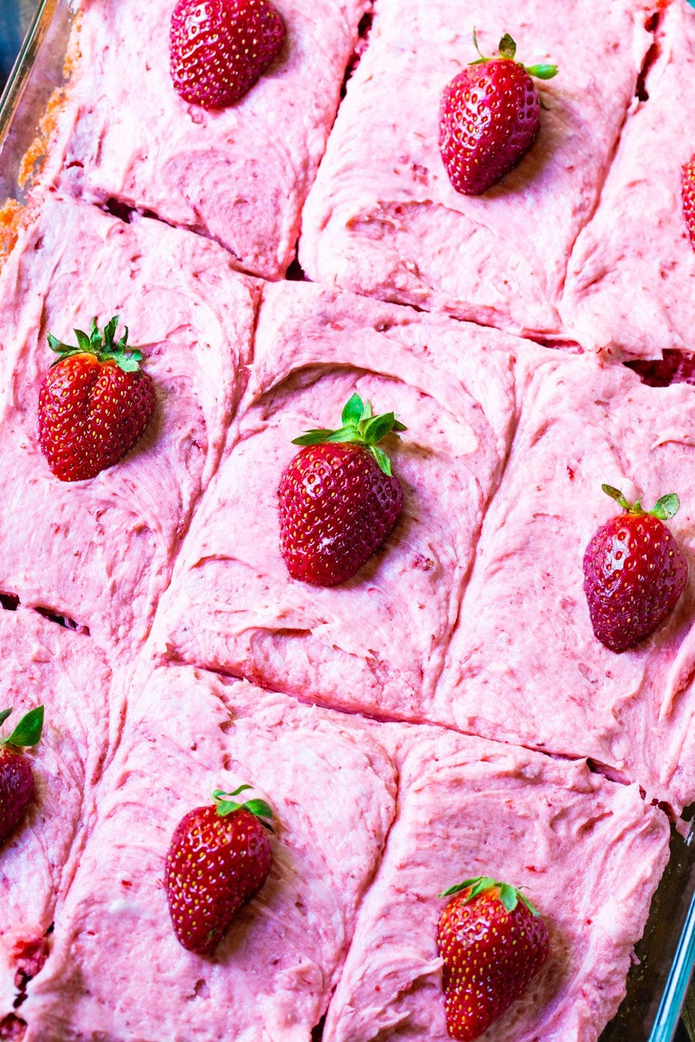 Sheet cake cut into squares in pan. Each one topped with a strawberry.