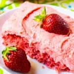 Slice of Strawberry Sheet Cake on a plate with a fresh strawberry.