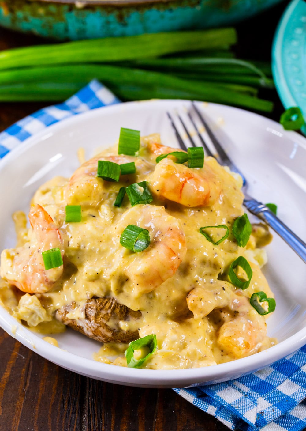 Stuffed Potato topped with cheesy seafood sauce and sliced green onions on a white plate.