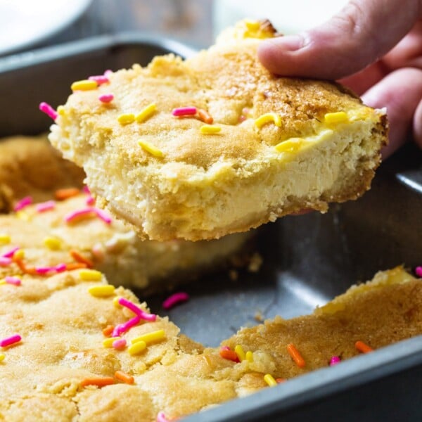 Hand lifting a Sugar Cookie Cheesecake Bar out of pan.