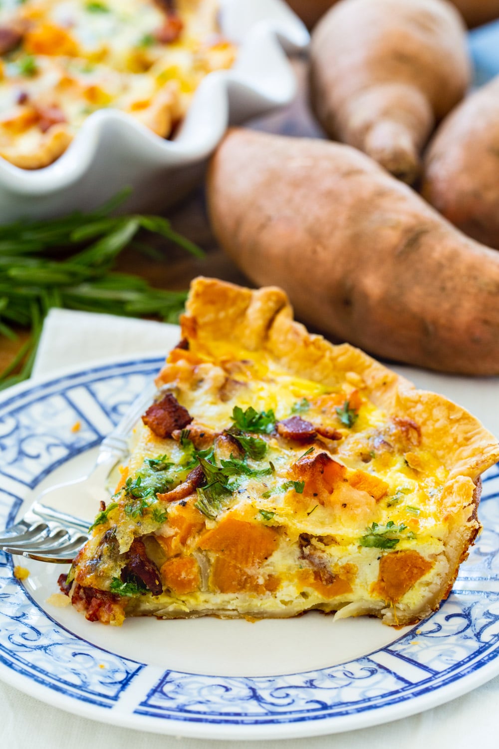 Slice of quiche with roasted sweet potatoes on blue and white plate.