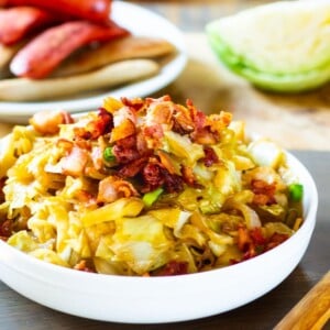 Cabbage in a bowl with plate of bratwurst in background.