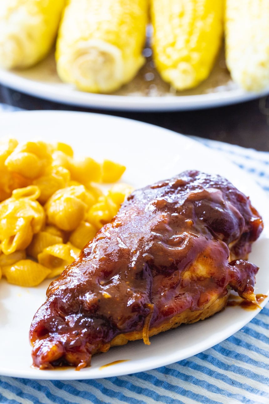 BBQ Chicken Breast on a plate with mac and cheese. Corn in background.