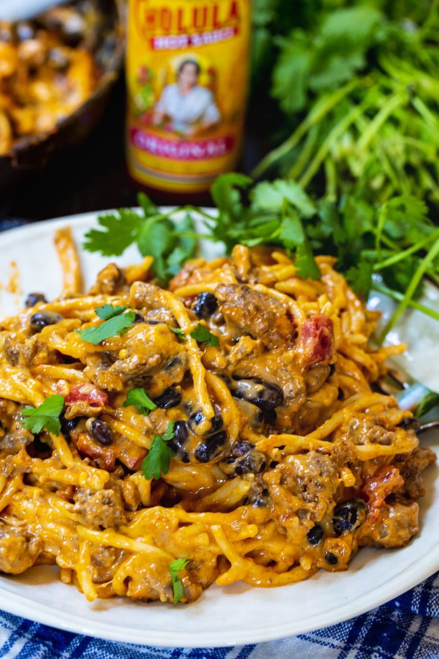 Taco Spaghetti on a plate with bottle of hot sauce and cilantro in background.