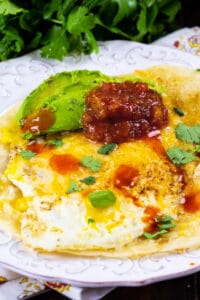 Tortilla Eggs topped with salsa and avocado on a plate.