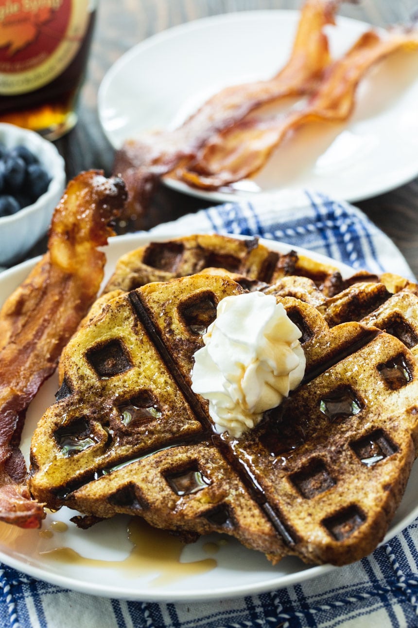 Waffled French Toast on a white plate with plate of bacon in background