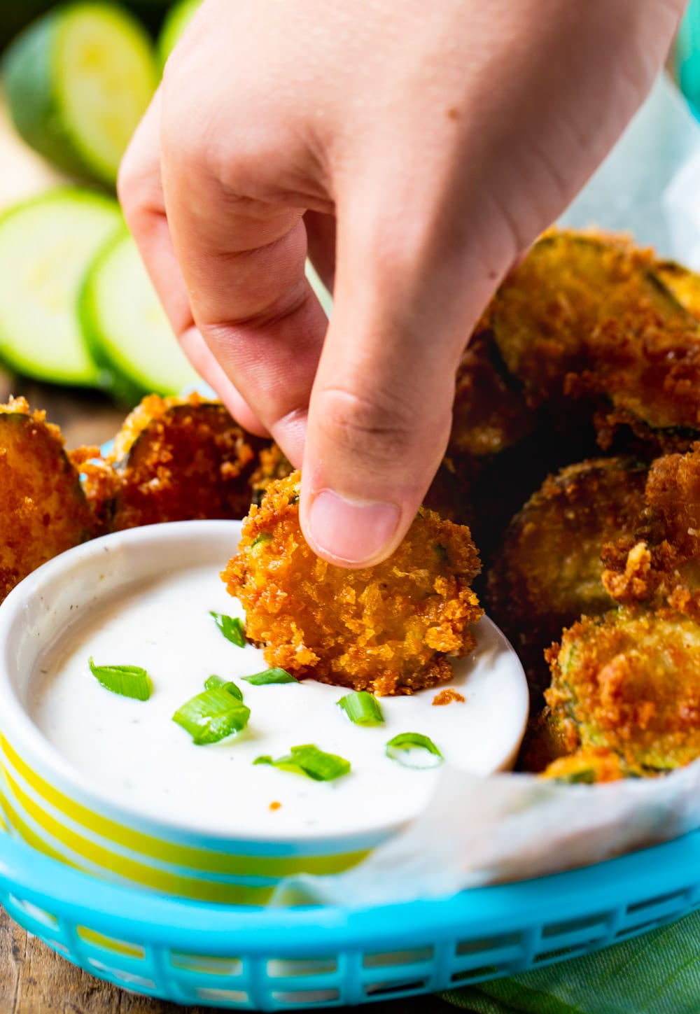 Hand dipping zucchini Chip in dip.