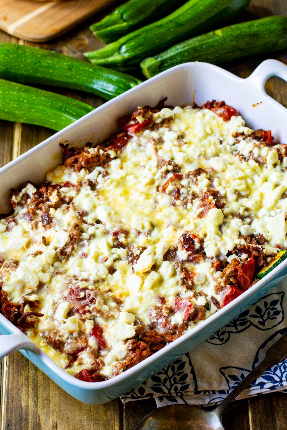 Moussaka in casserole dish with zucchini next to it.