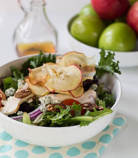 Ensalada en un bol con aderezo y bol de manzanas al fondo.