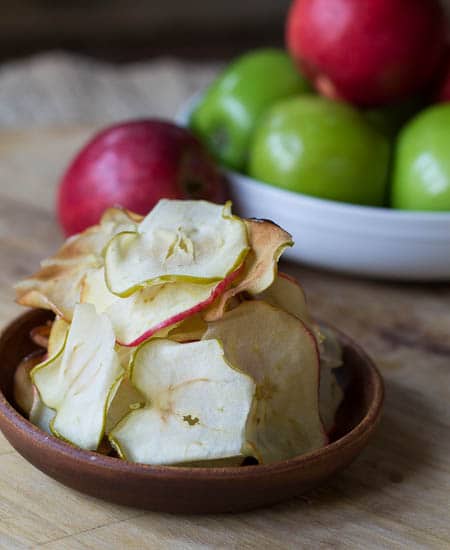 Caramelized Apple Chips on small plate with red and green apples in background.