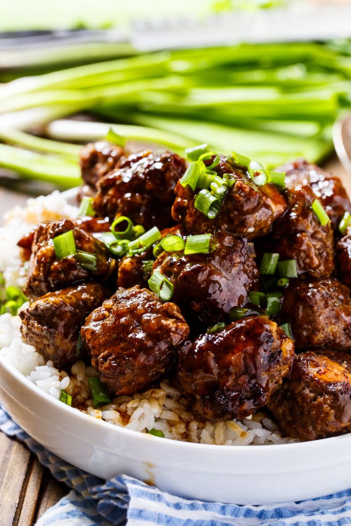 Glazed Meatballs served over white rice in a bowl with green onions in background.