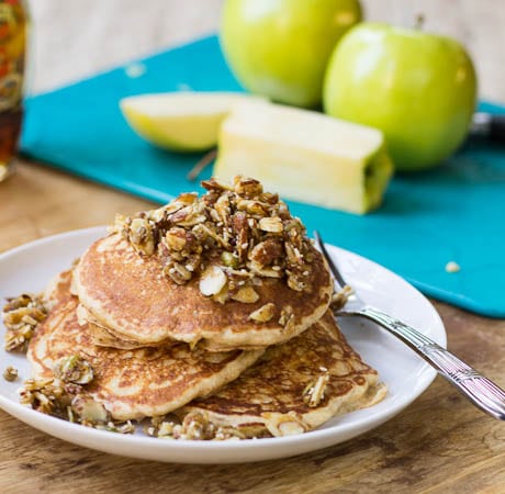 Apple Pancakes with Nutty Topping on a plate with Golden Delicious apples in background.