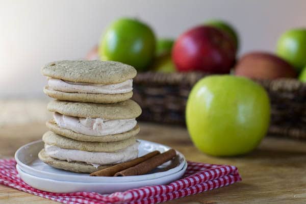 Apple Spice Whoopie Pies stacked on a small plate with apples in background.