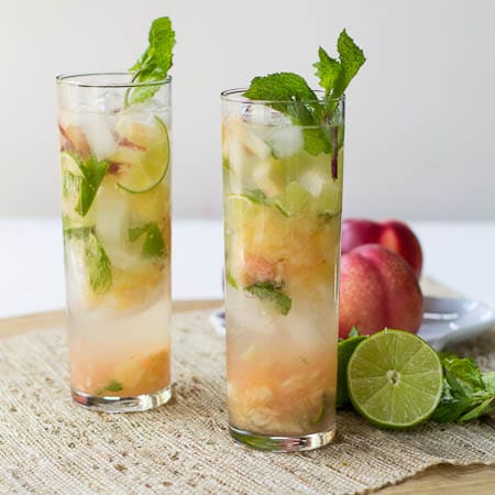 Nectarine Mojitos in tall glasses with lime halves and nectarines beside them.