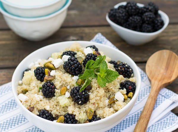 Quinoa Salad in white bowl with fresh blackberries in background.