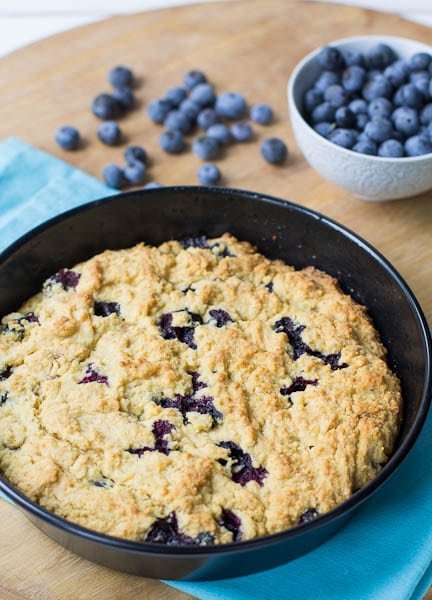 Blueberry Cornbread in a round cake pan with blueberries in background.