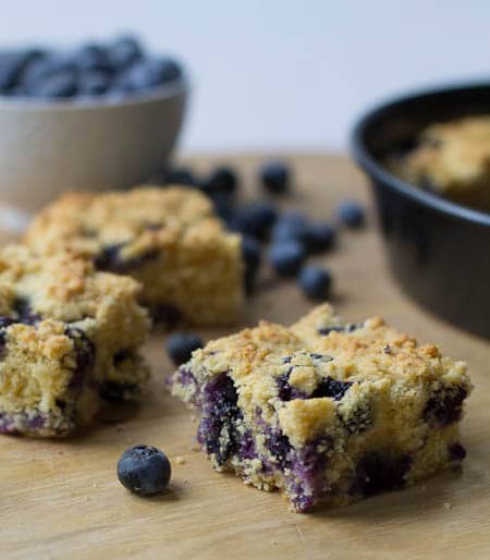Blueberry Cornbread cut into squares with bowl full of fresh blueberries.