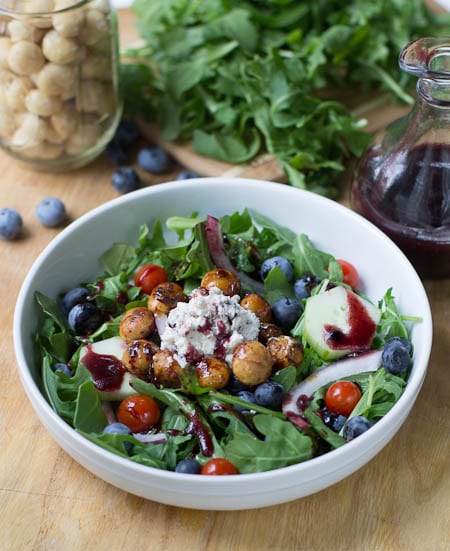 Blueberry Arugula Salad in white bowl with jar of macadamia nuts in background.