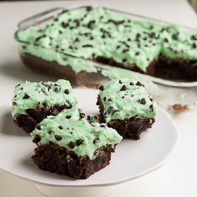 Thre brownies with mint frosting on a plate with baking dish full of brownies in background.