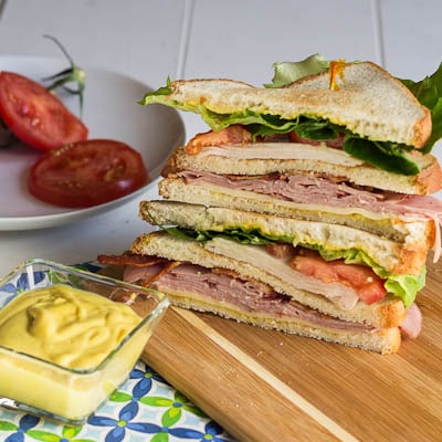 Stack of Club Sandwich halves on a cutting board with bowl of honey mustard.