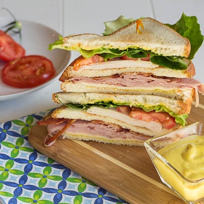 Club Sandwiches cut in half and stacked on a wood cutting board.