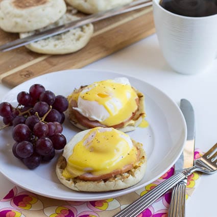 Eggs Benedict on a plate with red grapes.