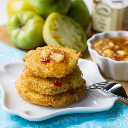 Stack Fried Green Tomatoes topped with pepper jelly sauce with green tomatoes in background.