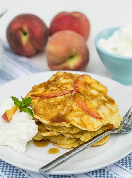 Sweet Peach Pancakes on a plate with fresh peaches in the background.