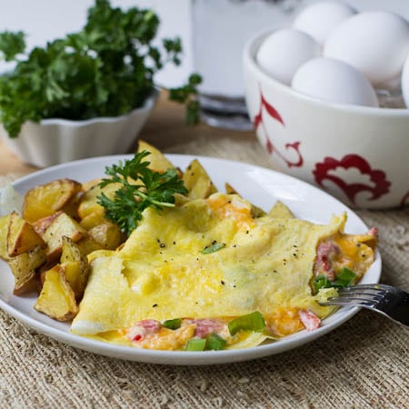 Omelet on plate with parsley and eggs in background.