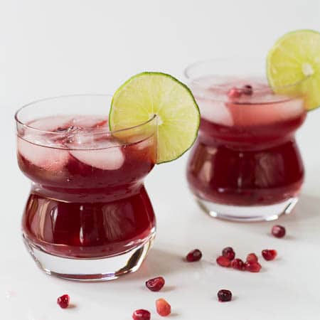 Two Pomegranate Margaritas with pomegranate seeds scattered around them.