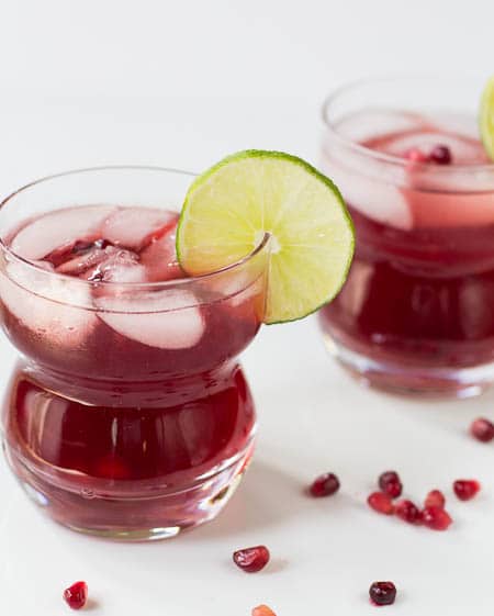 Two Pomegranate Margaritas with pomegranate seeds scattered around glasses.