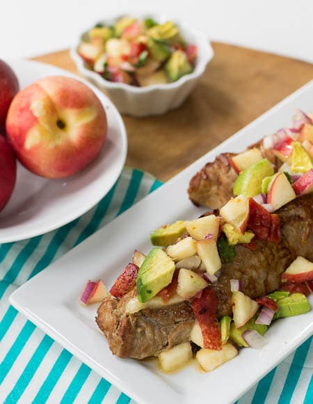 Pork Tenderloin with Nectarine Avocado Salsa on a serving plate with bowl of nectarines in background.