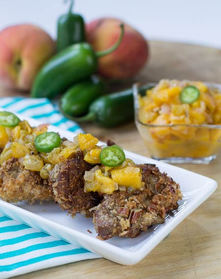 Pork Medallions topped with Spicy Peach Chutney on serving platter with peaches and jalapenos in background.