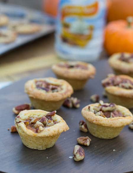 Pumpkin Tassies on a wood board with pecans scattered around them.