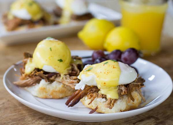 Eggs Benedict on a white plate with red grapes beside it.