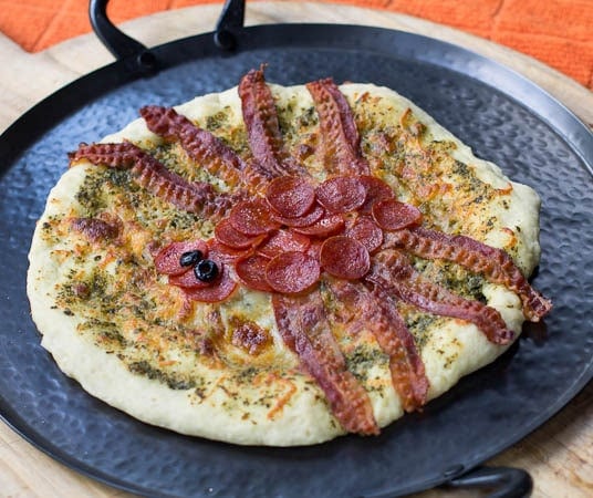 Whole pizza with pepperoni forming body of spider and bacon legs.