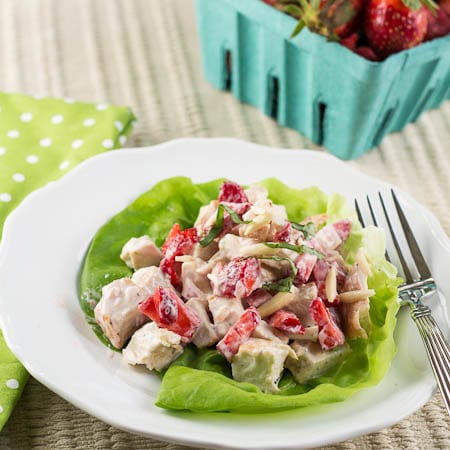 Chicken Salad with Strawberries served on a leaf of lettuce with a basket of strawberries.