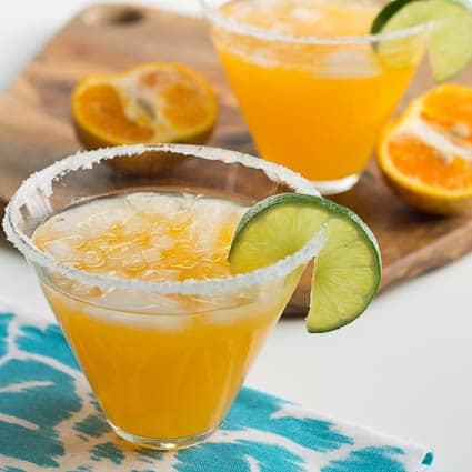 Tangerine Margarita in a glass with orange halves in background.