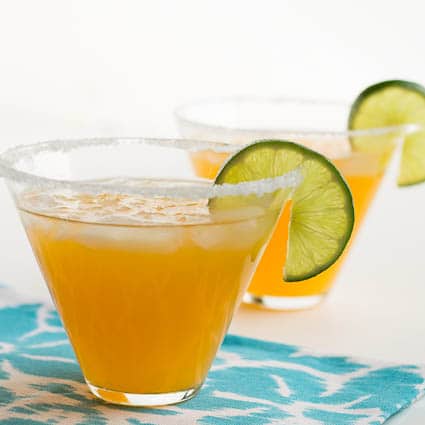 Tangerine Margaritas in glasses with lime wedges.