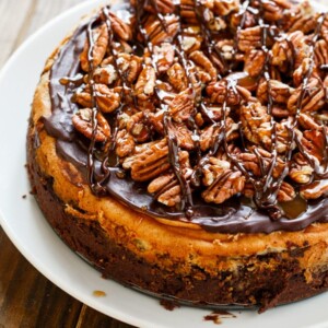 Turtle Brownie Cheesecake with a brownie crust and pecans, caramel sauce, and chocolate sauce.