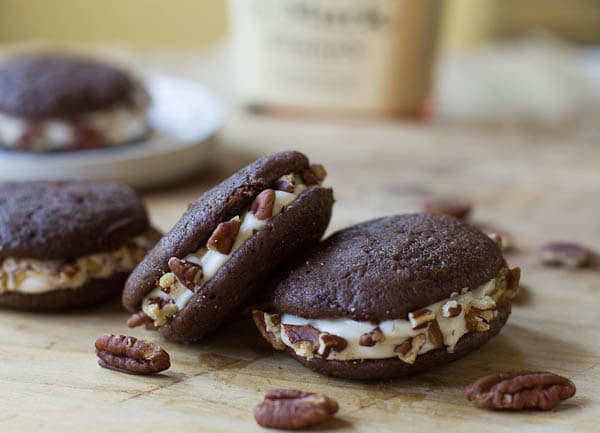 Whoopie Pies on a wood cutting board with pecans scattered around them.